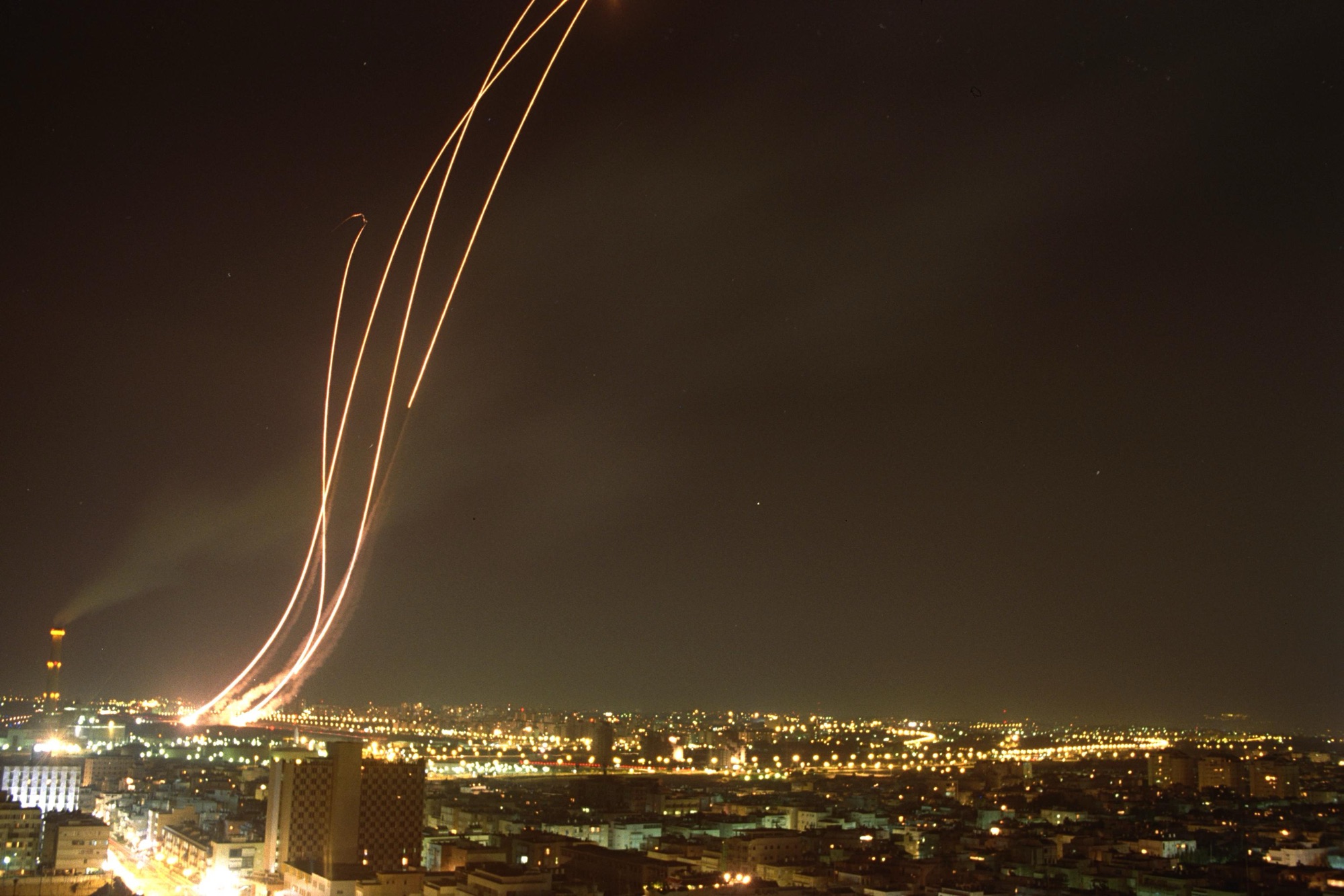 Multiple missile interception trajectories glowing in the night sky over a city